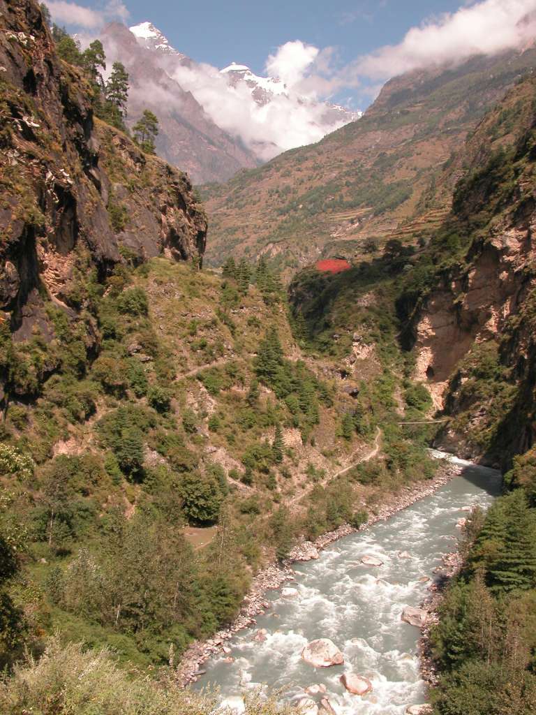 Manaslu 05 06 Buri Gandaki Bridge To Rana With Lapuchun and Dwijen Himal A short distance beyond Deng the trail crosses the Buri Gandaki onto what is now the north bank, and climbs to Rana (1980m). The red vegetation on the far bank is buckwheat. In the distance to the north on the Tibetan border are Lapuchun (5960m) and Dwijen Himal (5521m).